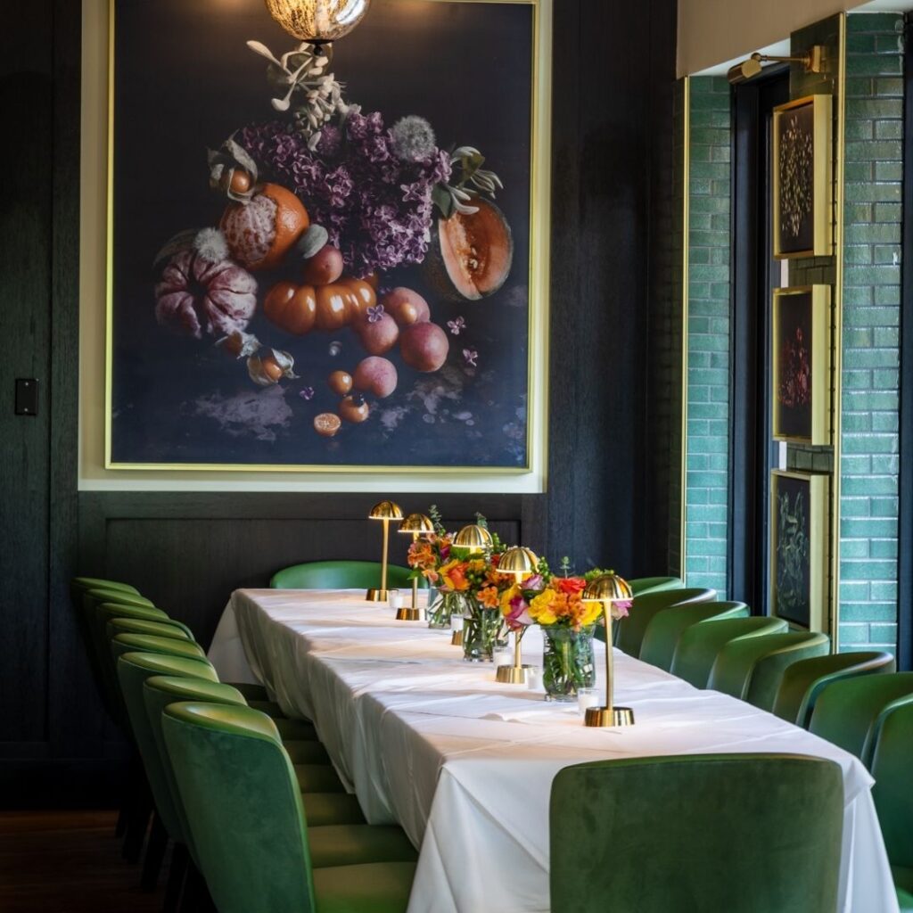 Private event dining table at The Bellevue Chicago with green velvet seating, gold candlesticks, floral arrangements, and dramatic still life artwork