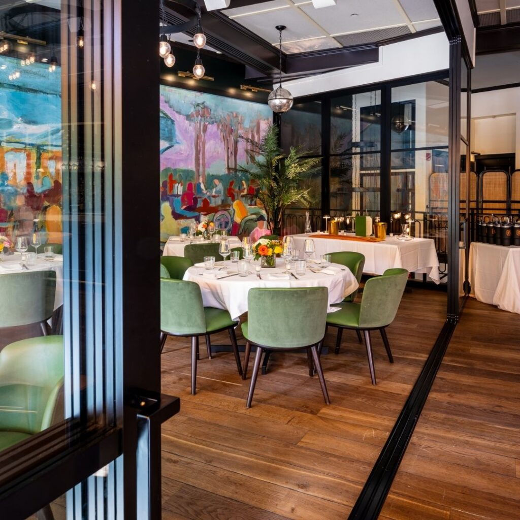 Private dining room at The Bellevue Chicago featuring round tables with white linens, green velvet chairs, and a colorful mural